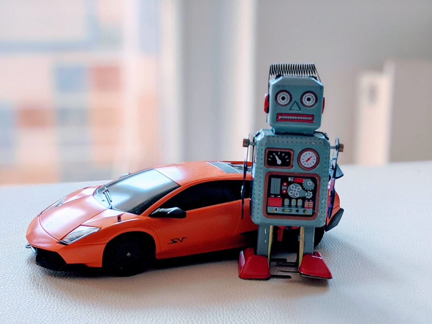 The vintage blue tin wind-up robot standing beside an orange toy sports car